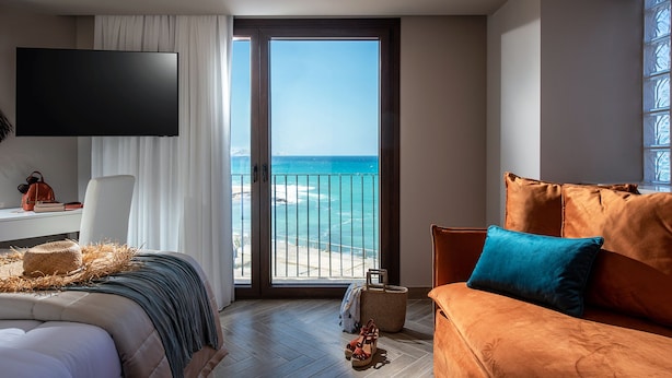 Une chambre d’hôtel moderne dotée d’un grand balcon, d’un lit offrant une belle vue, d’une télévision à écran plat et d’un coin salon confortable.