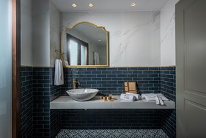 Uma casa de banho com lavatório de mármore, azulejos azul escuro nas paredes, espelho com moldura dourada e bancada branca.