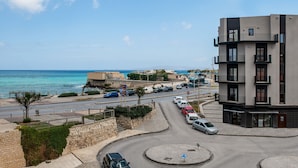Une route côtière avec un rond-point, un bâtiment moderne doté de balcons et une vue sur la mer.