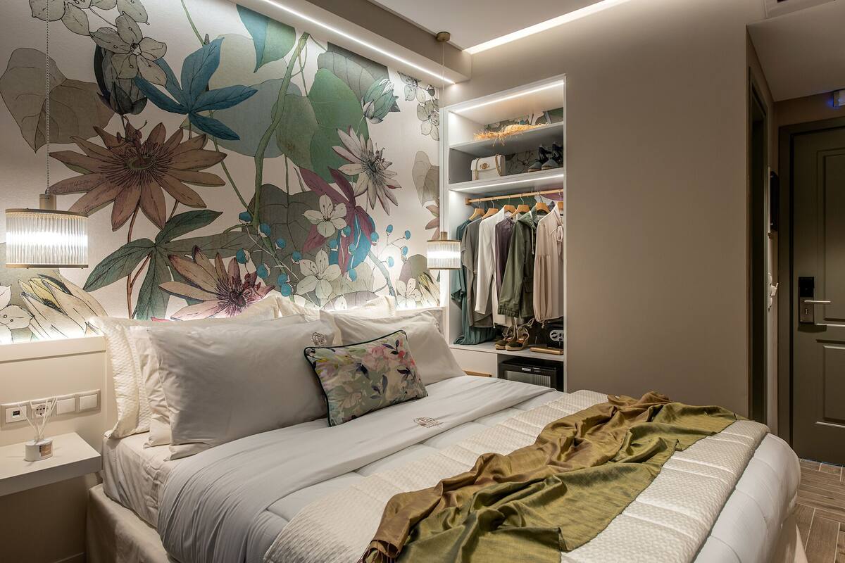 A modern bedroom with a large floral mural, a neatly made bed with a green throw, and a walk-in closet with hanging clothes.
