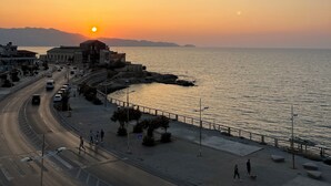 Une route côtière offrant une vue sur le coucher de soleil, une promenade piétonne et une mer calme.