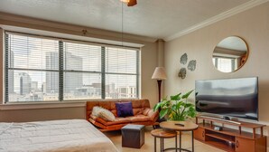 A modern living room with a large TV, a sofa, a coffee table, and a city view through the window. - Downtown Jacksonville Studio w/ City Views! (Jacksonville)