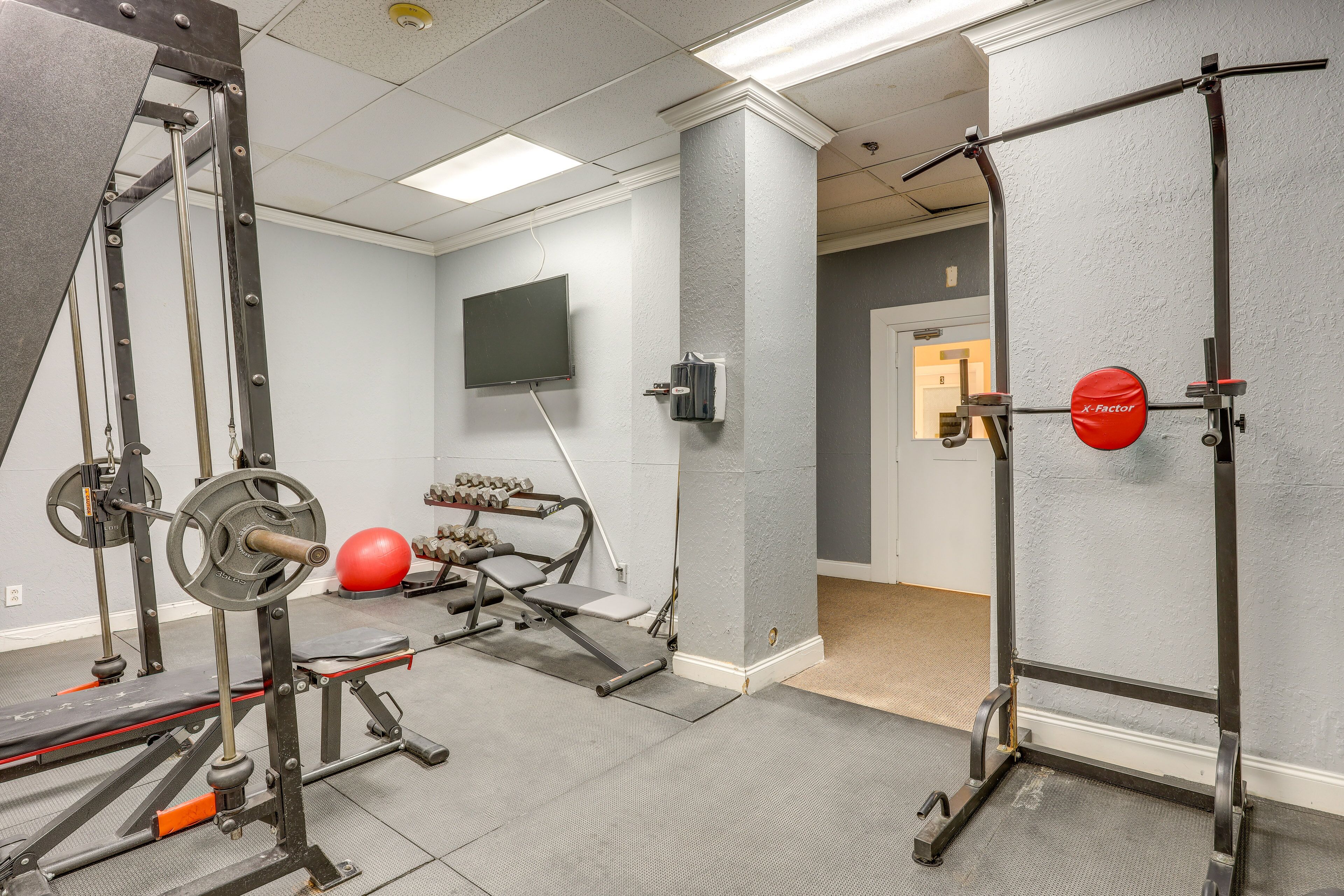 A gym with weightlifting equipment, a television, and a red exercise ball.