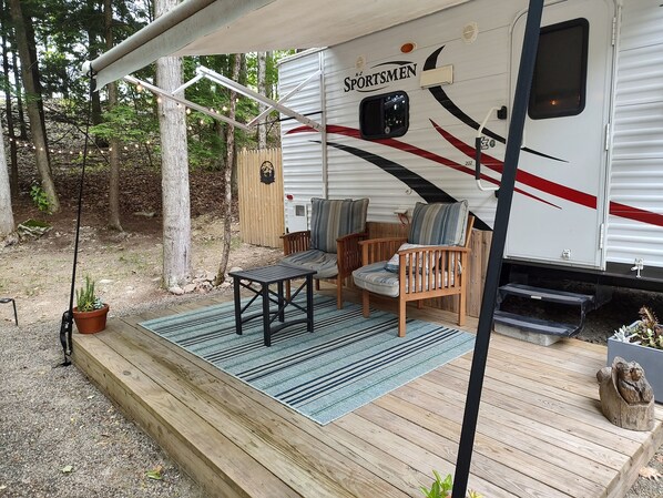 A covered outdoor area with a wooden deck, two chairs, a table, and a potted plant.