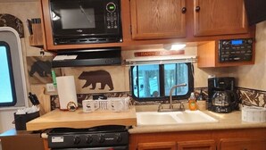 A compact kitchen with a microwave, stove, sink, and wooden cabinets. - Get away and get back to nature! (East Nassau)