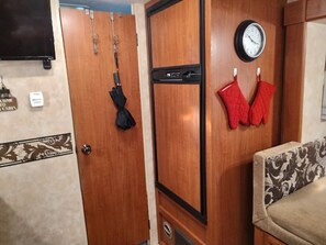 Een houten deur met een zwarte hendel, een klok en rode ovenwanten aan de muur.