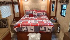 A cozy RV bedroom with a quilted bedspread featuring animal prints, a wooden headboard, and a small bench with folded towels. - Get away and get back to nature! (East Nassau)