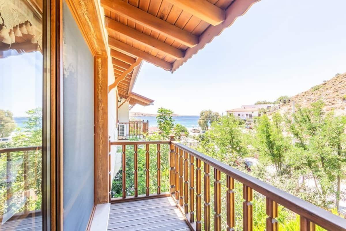 A balcony with a wooden railing, a view of the sea, and buildings in the background.