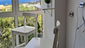Une pièce avec une table et des chaises, un luminaire suspendu, une plante en pot posée sur une étagère et une vue sur le paysage, visible à travers de grandes fenêtres.