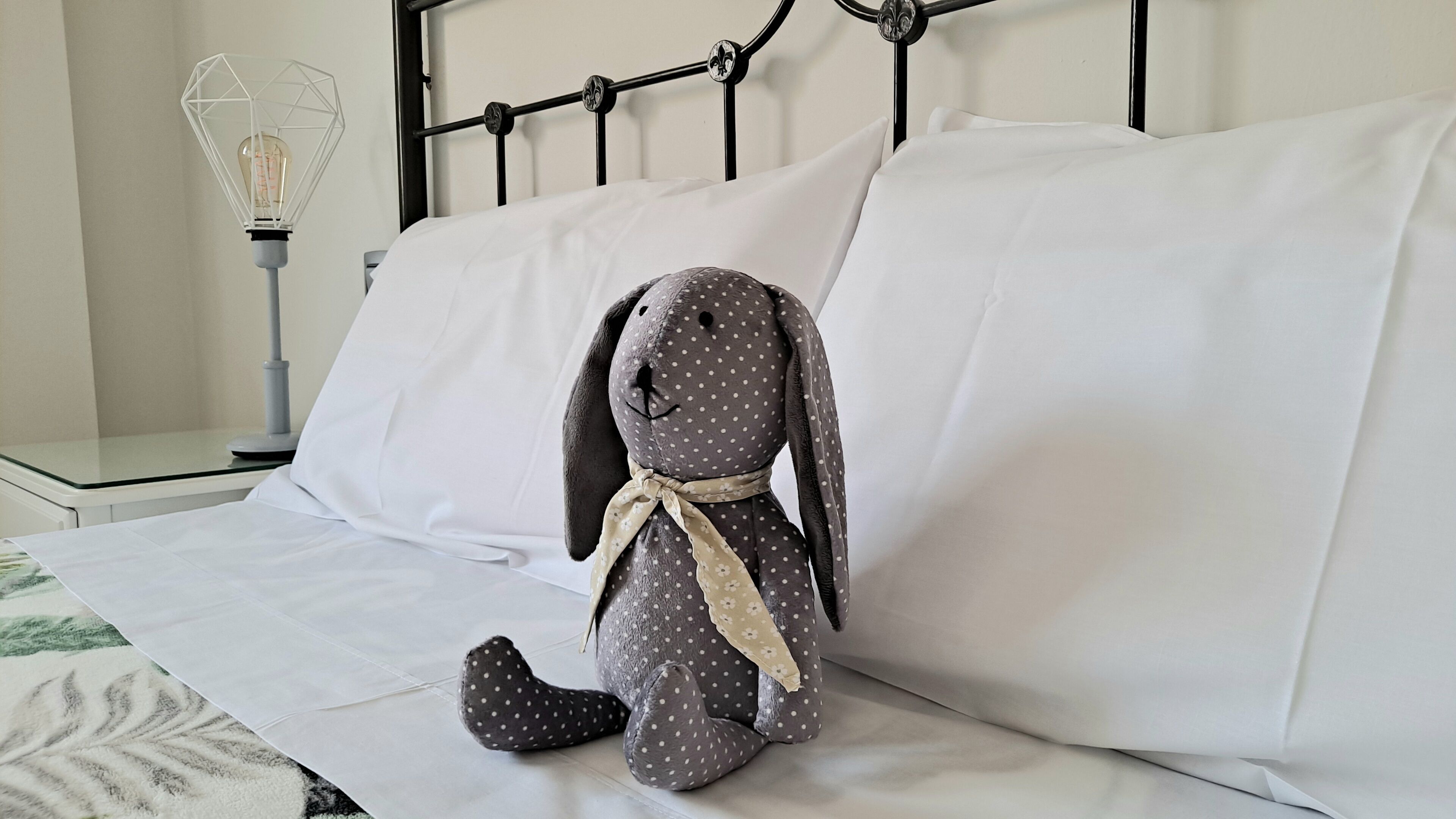 A bed with white linens, a metal headboard, and a plush bunny toy on the bed.