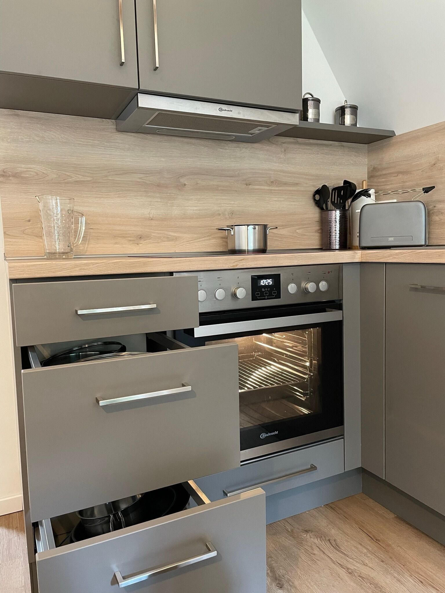 A modern kitchen with a built-in oven, stainless steel appliances, and wooden cabinetry.