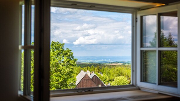 Une pièce dotée d’une grande fenêtre donnant sur un paysage rural, avec des arbres et des éoliennes visibles au loin.