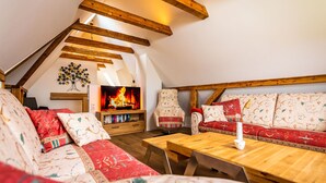 Une pièce mansardée chaleureuse avec un plafond en bois, une cheminée, un ensemble de canapés et une table basse en bois.