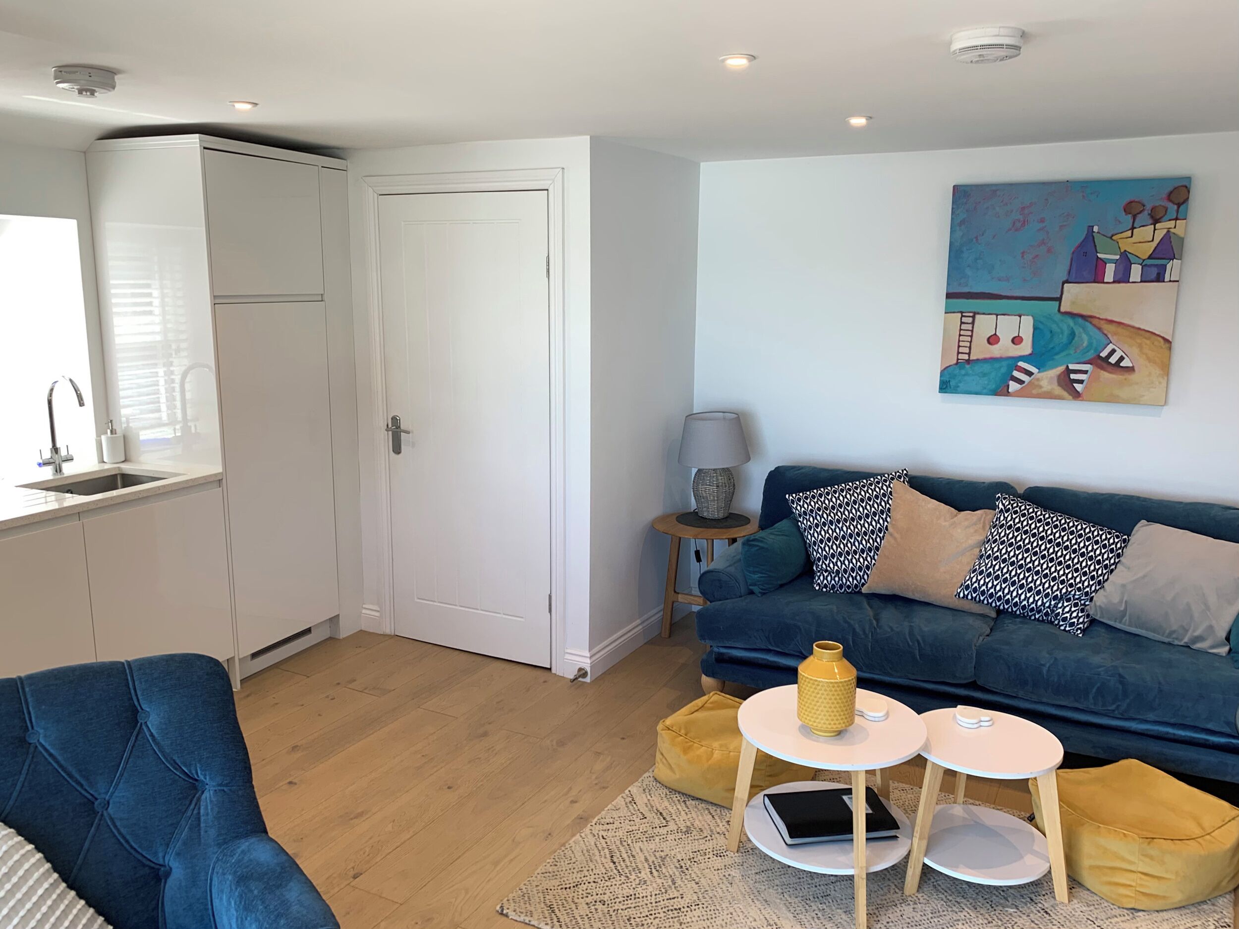 A modern living room with a blue sofa, a small round table, a yellow bean bag, and a painting on the wall.