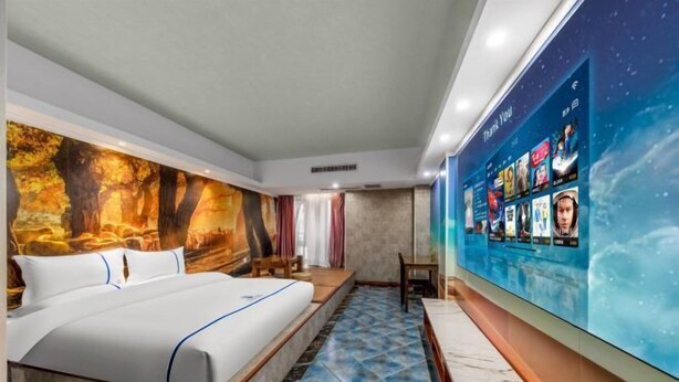 A hotel room with a large bed, a mural on the wall, and a digital screen displaying movie titles. - Chongqing Tianfei Art Hotel (Olympic Sports Center Yuanjiagang Subway Station) (Chongqing)