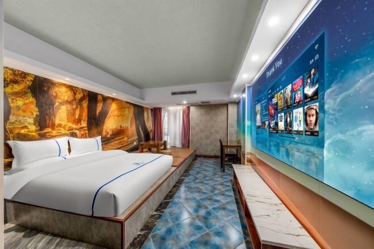 A hotel room with a large bed, a mural on the wall, and a digital screen displaying movie titles.