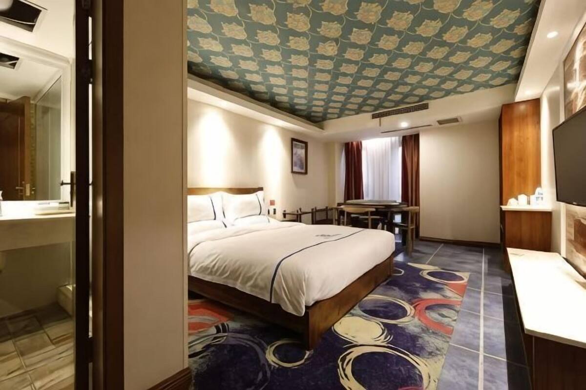 A hotel room with a bed, a desk, a mirror, and a television.