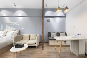 A modern hotel room with a bed, a sofa, a small table, and a kitchenette.