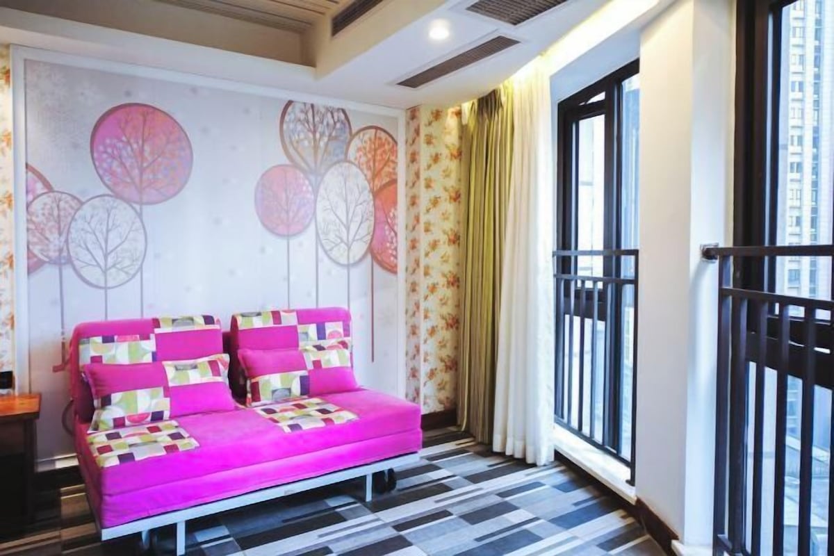 A room with a pink sofa, patterned cushions, a wall with circular designs, a window with curtains, and a patterned floor.