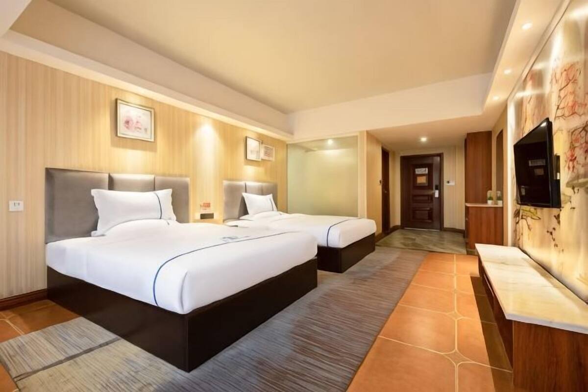 A hotel room with two beds, a TV, a desk, and a bathroom.