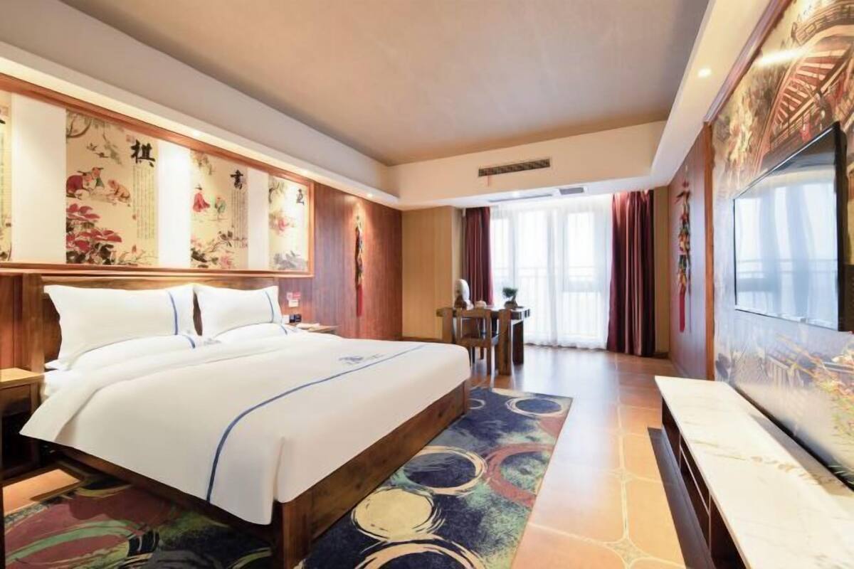 A hotel room with a large bed, a wooden headboard, a dining table, and a TV.