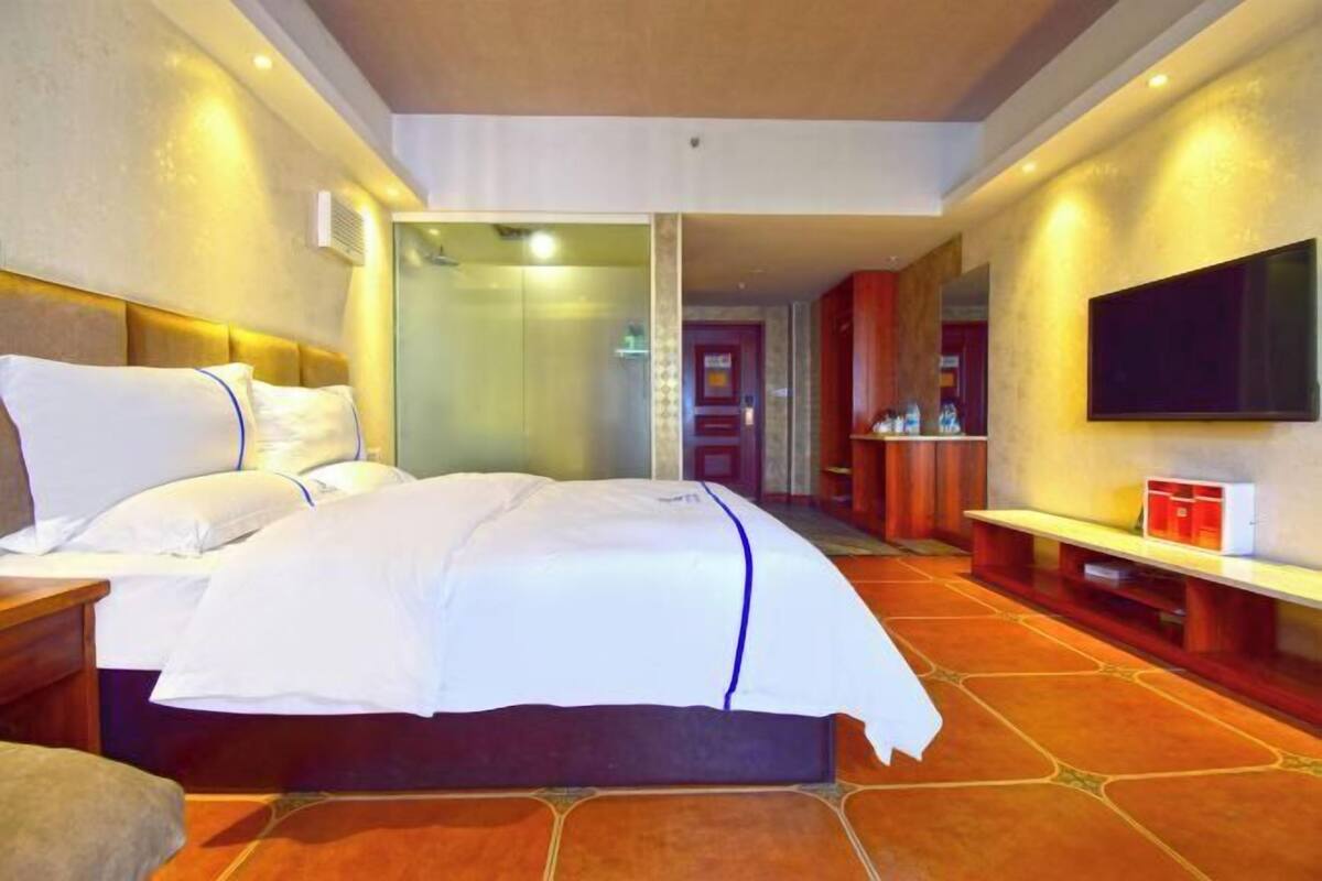 A hotel room with a large bed, a TV mounted on the wall, and a bathroom visible through a glass door.