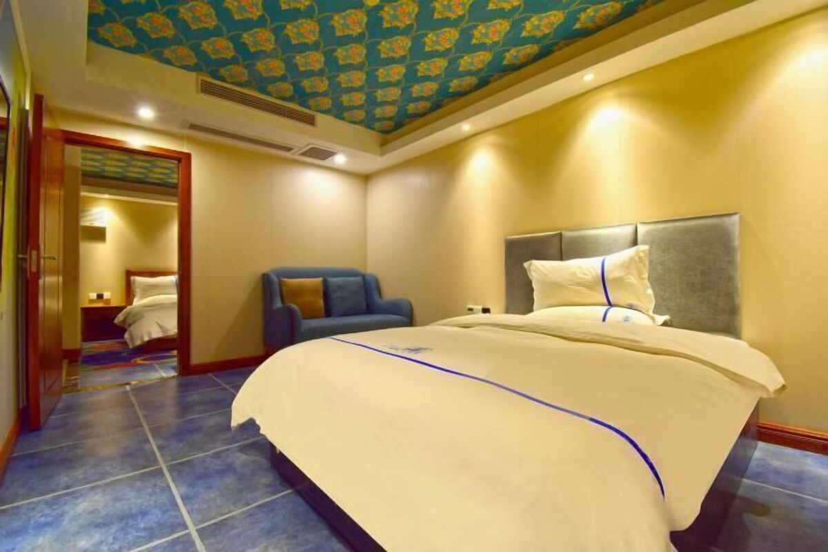 A hotel room with a large bed, a chair, a mirror, and a patterned ceiling.