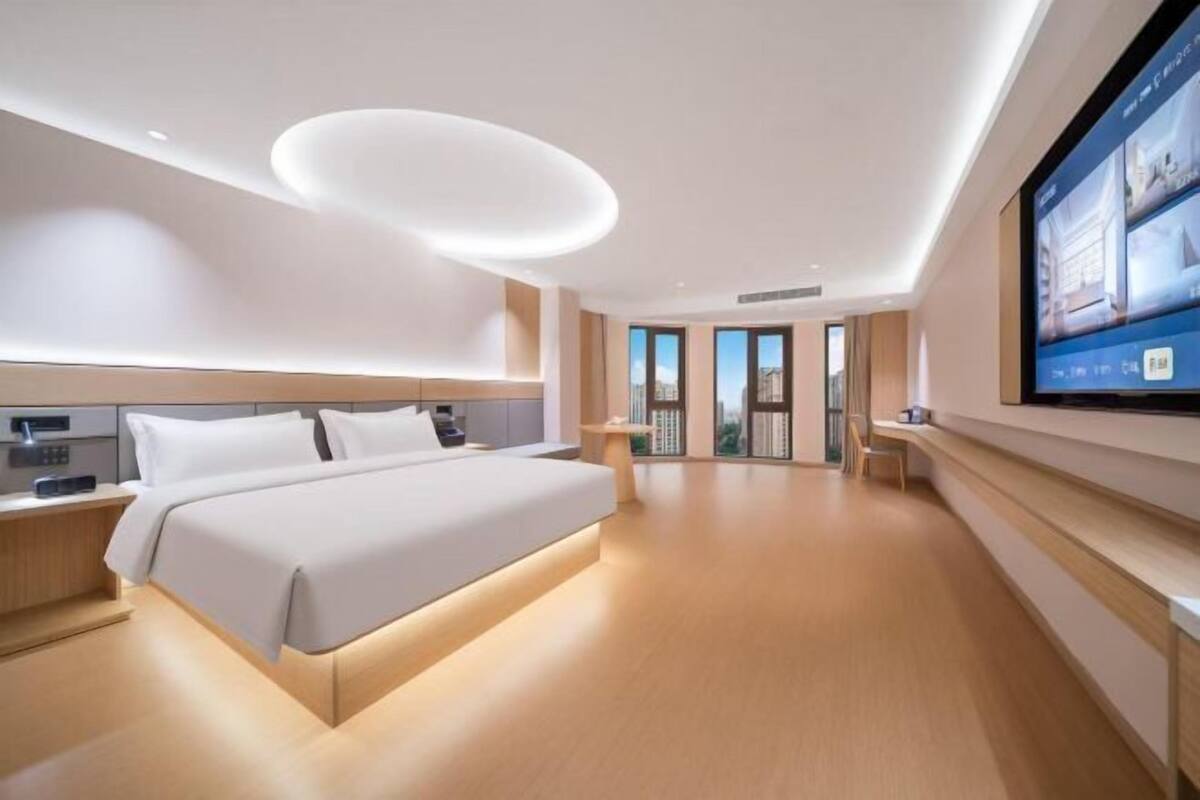 A modern hotel room with a large bed, a flat-screen TV mounted on the wall, and a balcony with a view.