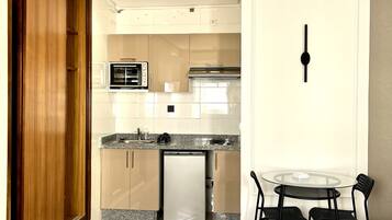 Habitación de hotel compacta con kitchenette, zona de comedor con mesa y sillas, y una cama grande.