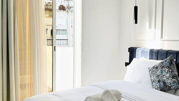 A hotel room with a large bed, a window with curtains, an air conditioning unit, and a view of buildings outside.