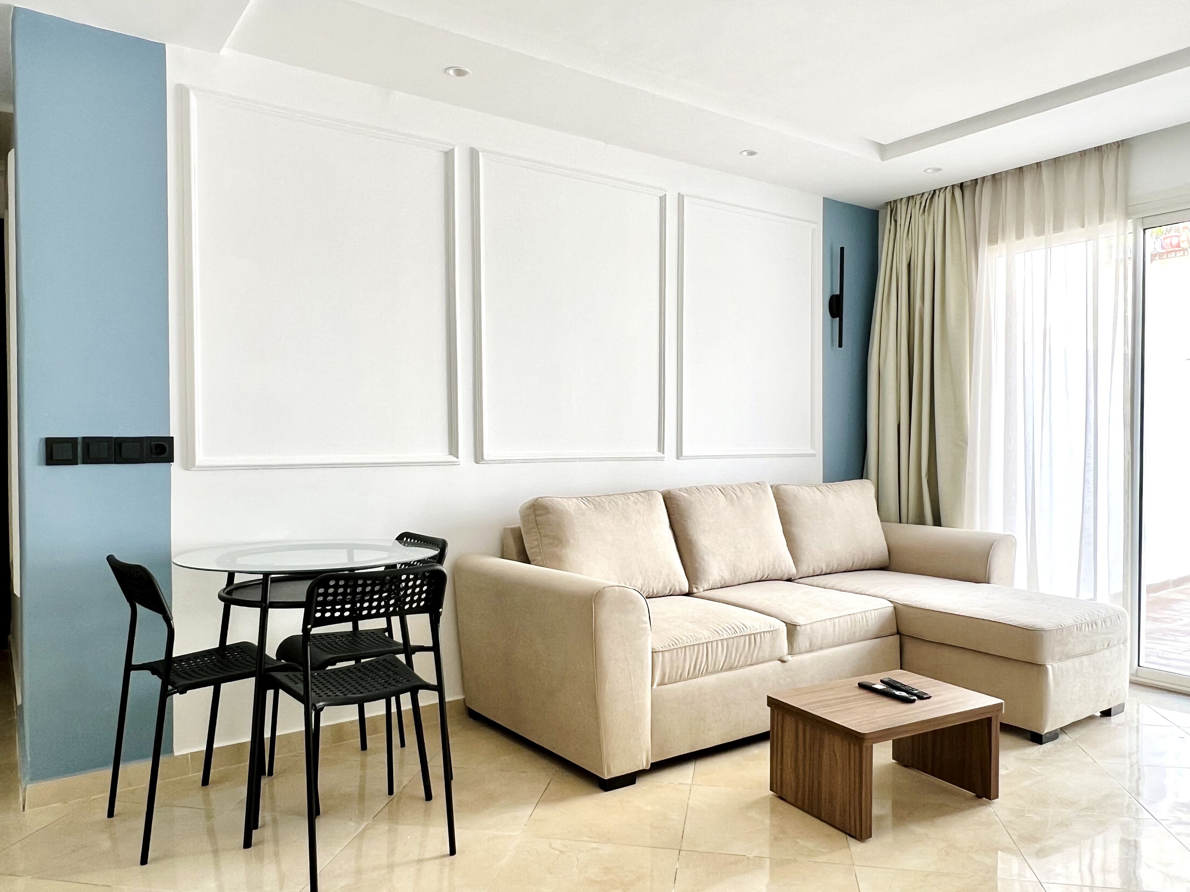 Una sala de estar moderna con un sofá seccional color crema, una mesita redonda pequeña, dos sillas negras y una mesa de centro de madera.