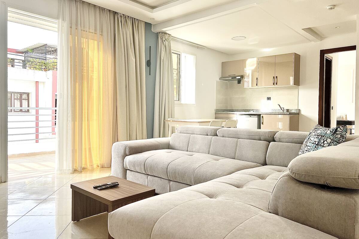 Una sala de estar moderna con un sofá modular, una mesa de centro y una cocina al fondo.