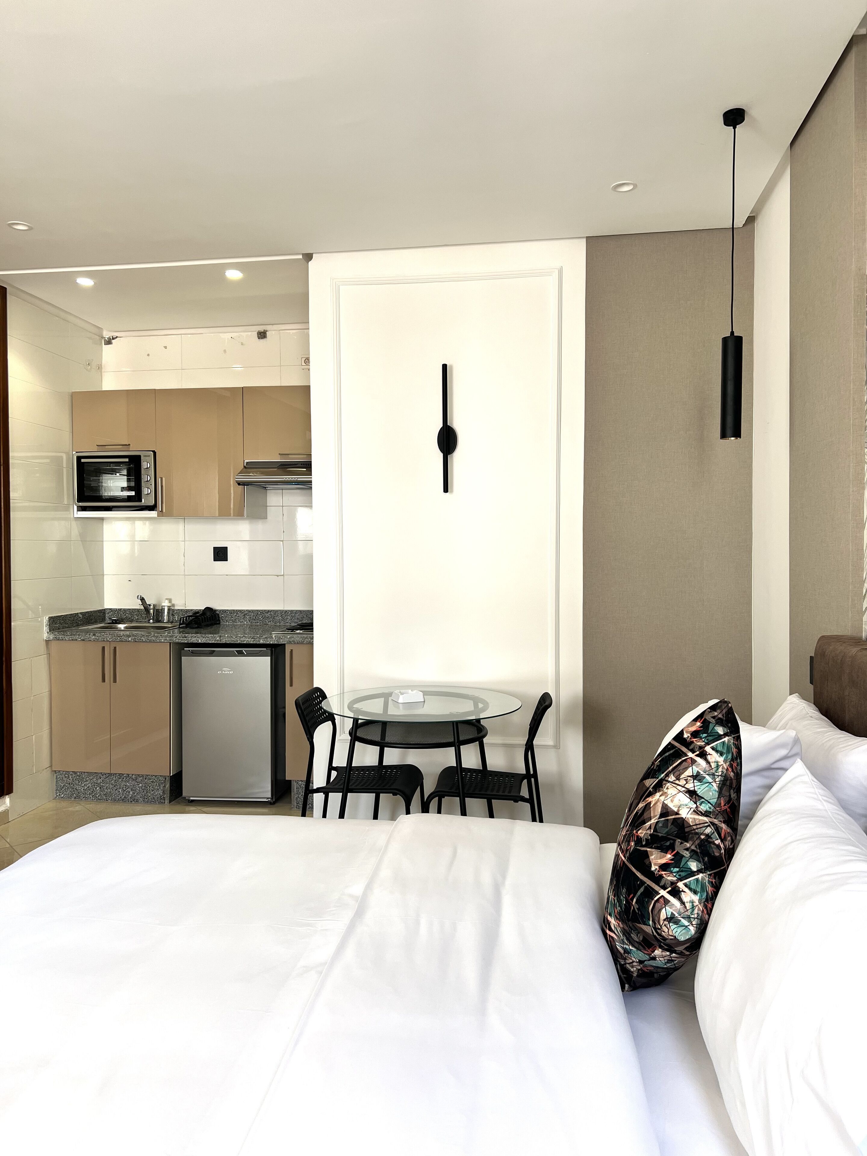 A hotel room with a bed, a small dining table with chairs, a microwave, a refrigerator, and a kitchen area with cabinets and a sink.