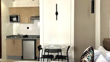 A hotel room with a bed, a small dining table with chairs, a microwave, a refrigerator, and a kitchen area with cabinets and a sink.