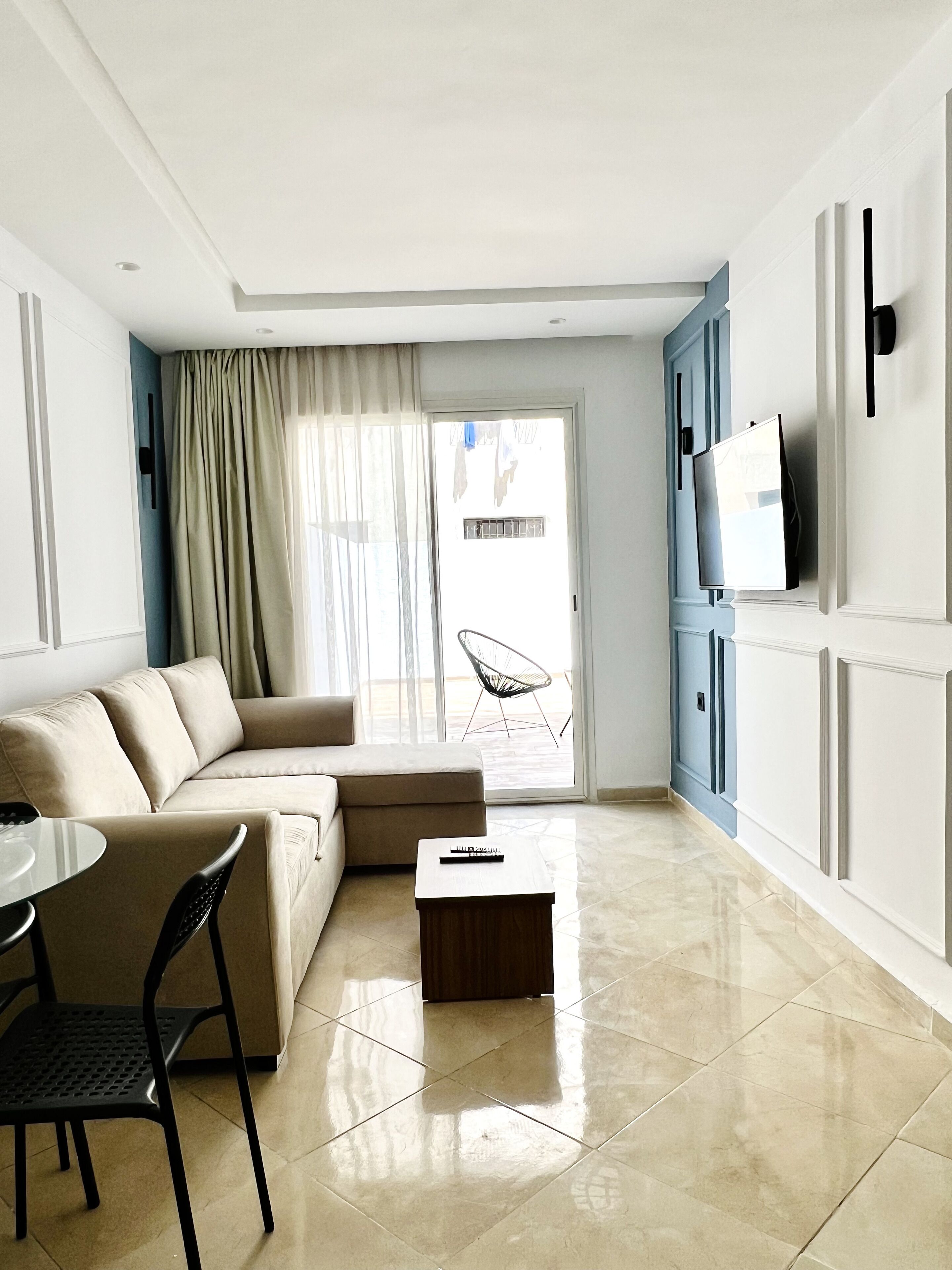 Una sala de estar moderna con un sofá color beige, una mesa de centro de madera y un televisor montado en la pared.