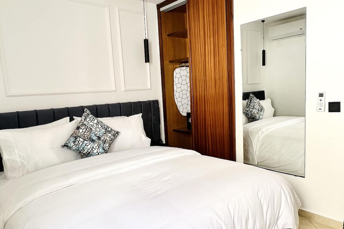 Una habitación de hotel moderna con una cama grande, un armario de madera, un espejo y una mesita de noche.