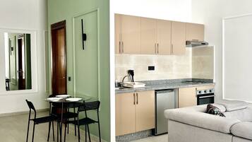 A modern bedroom with a bed, a dining table with chairs, a kitchenette with cabinets, and a grey sofa.