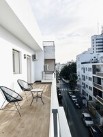 Varanda com duas cadeiras e uma mesa, com vista para uma rua com carros estacionados e edifícios.