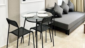 A modern living room with a round glass table, black chairs, a grey sofa with cushions, and two wall-mounted light fixtures. - MyCity (Rabat)