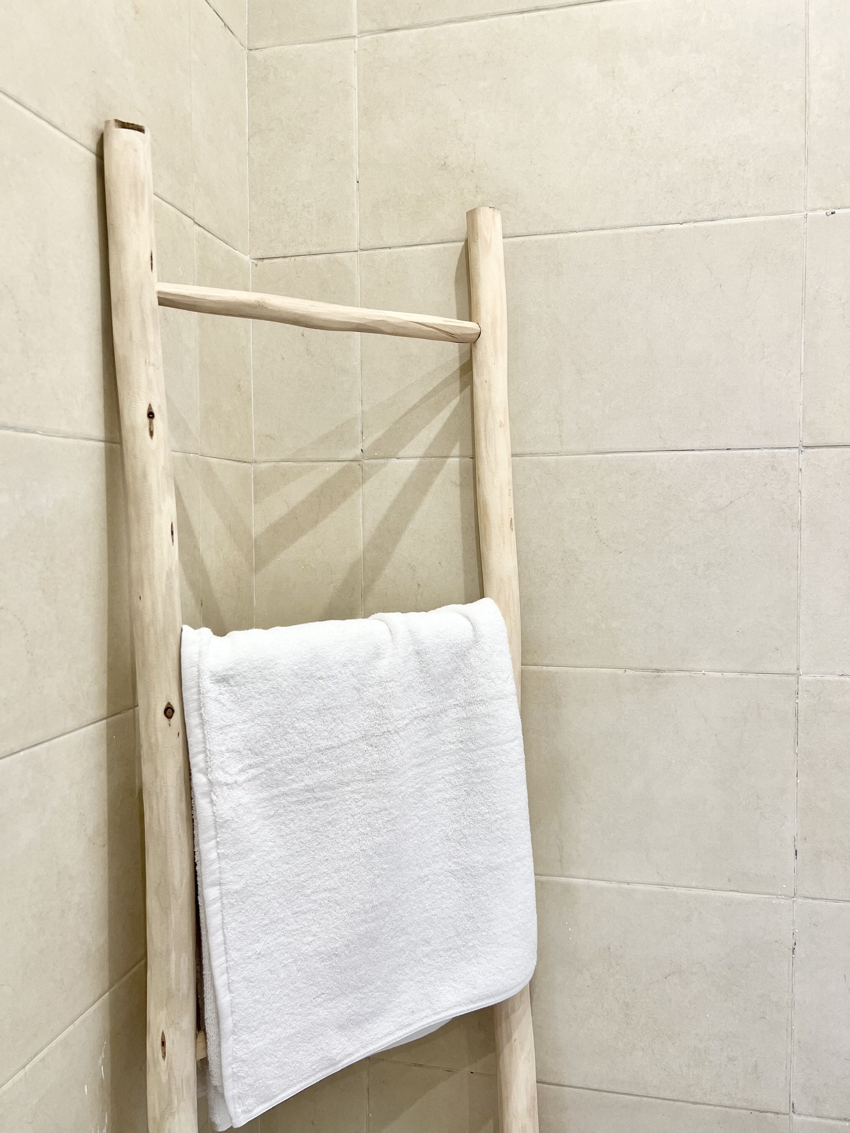 Una escalera de madera con una toalla blanca colgada, apoyada contra una pared azulejada.