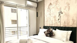 A hotel room with a bed, a window with curtains, an air conditioning unit, and a wall with a nature-themed mural. - MyCity (Rabat)