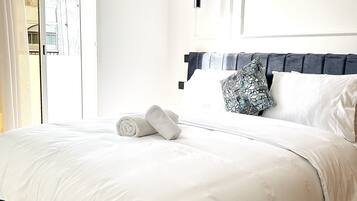 A neatly made bed with white linens, a dark headboard, and a patterned pillow.