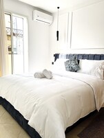 Una cama bien hecha con sábanas blancas, cabecera oscura y un cojín estampado.