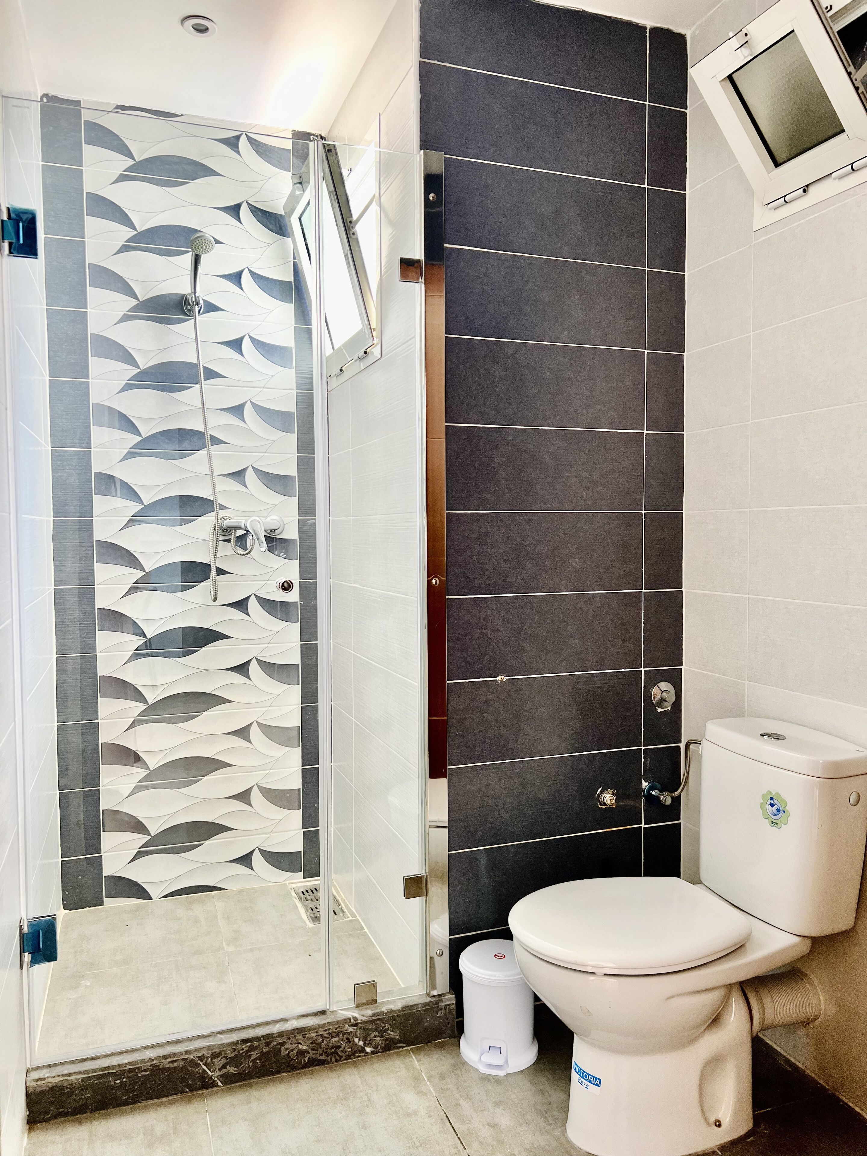 A bathroom with a shower enclosure, a toilet, and a wall-mounted window.