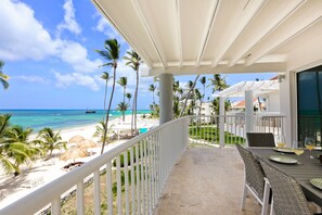 Ein Balkon mit Blick auf Strand und Meer, Korbmöbel und ein Tisch mit Gläsern.