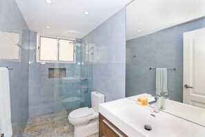 Ein modernes Badezimmer mit einer gläsernen Duschkabine, einer weißen Toilette und einem großen Spiegel über dem Waschbecken.
