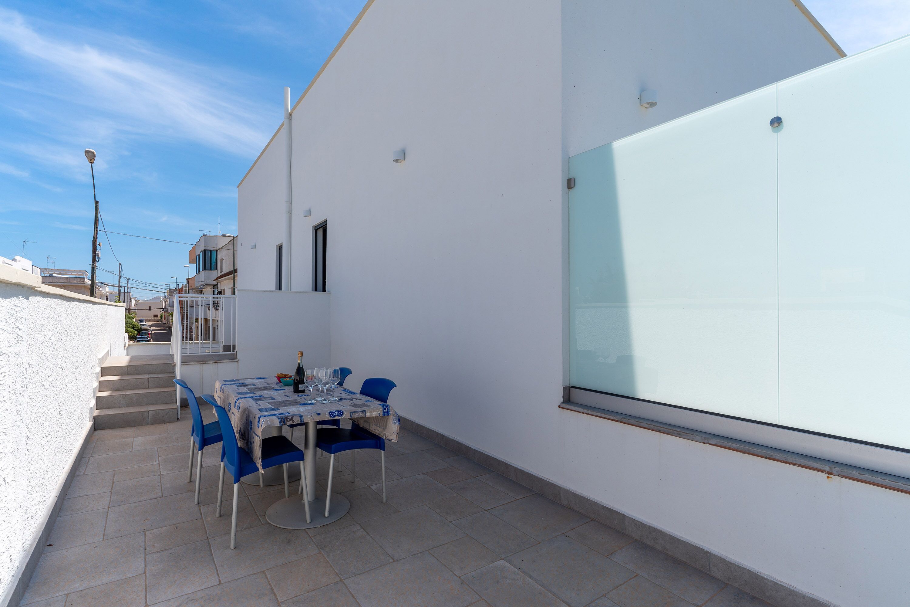 A patio with a table and chairs, a white wall, and a glass door.