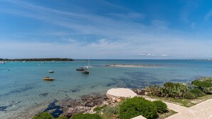 Vista costera con barcos en aguas turquesas cristalinas, costa rocosa y vegetación.