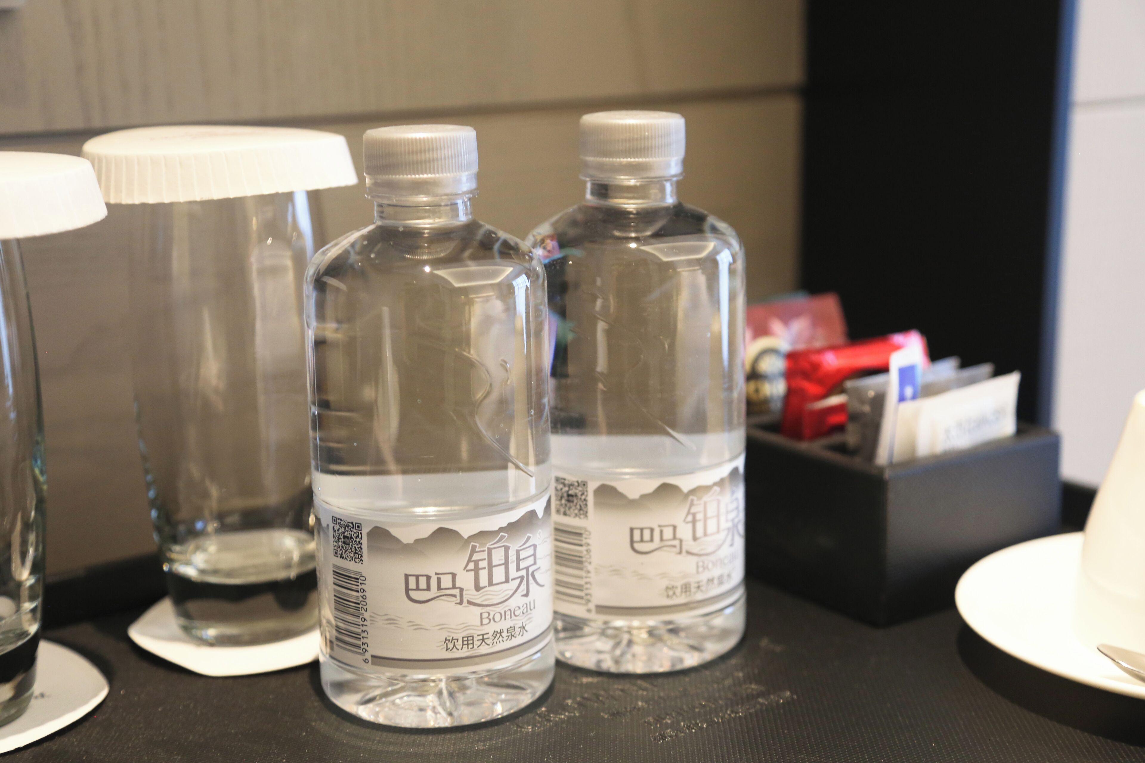 Two bottles of water labeled "Bateau" on a table with a black surface, a white cup, and a black box with items.