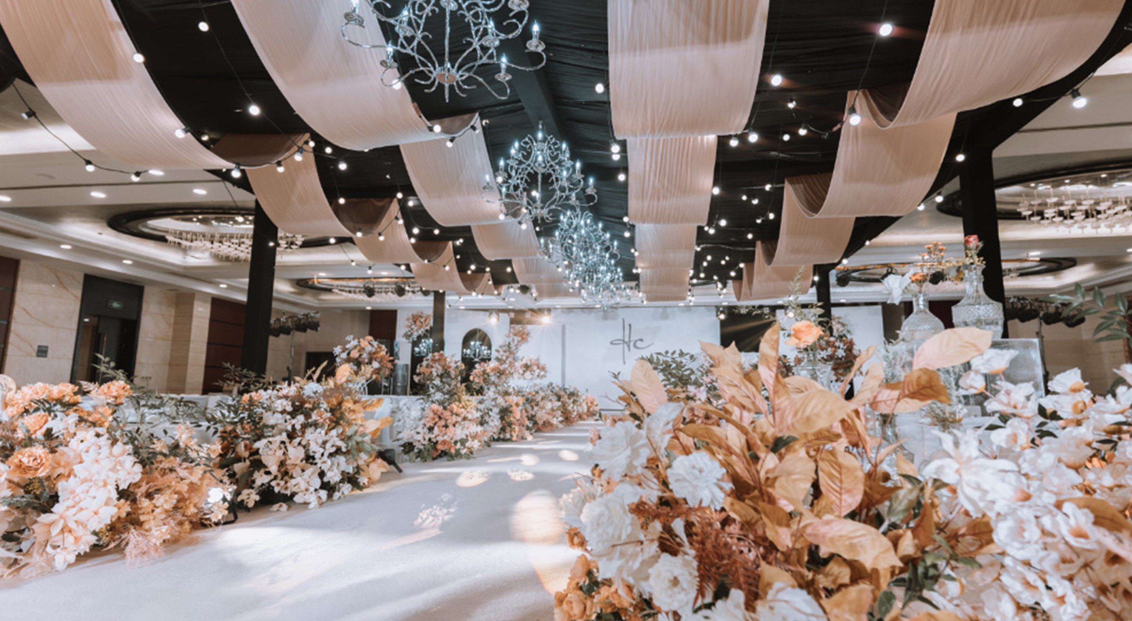Ein geräumiger Saal mit floral geschmücktem Gang, Kronleuchtern und weißem Hintergrund.
